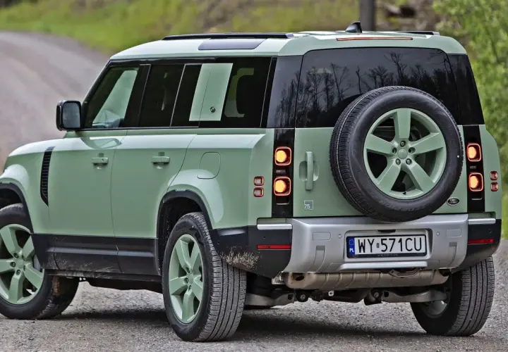 Zielony Land Rover Defender na szutrowej drodze, gotowy na przygodę.