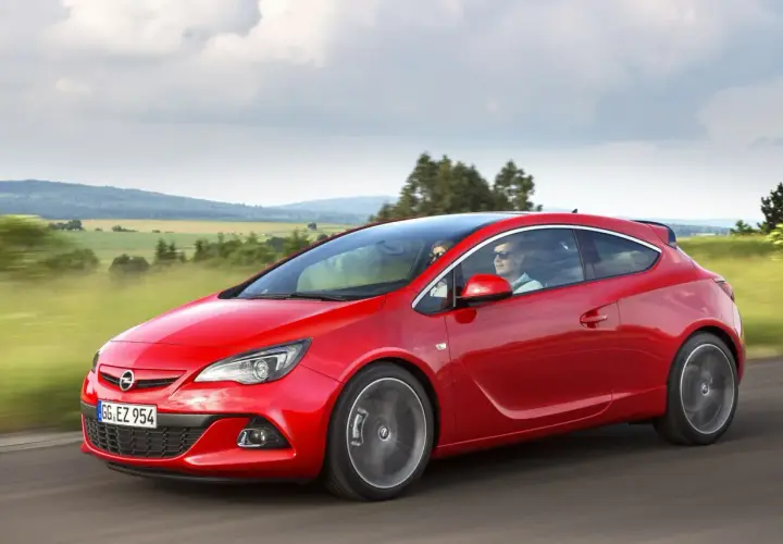 Czerwony Opel Astra J Hatchback pędzi przez malownicze krajobrazy.