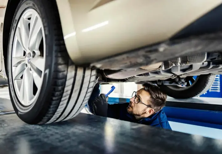 Mechanik z latarką bada podwozie samochodu.