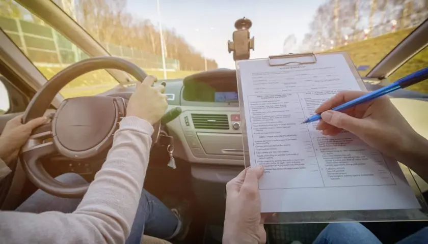 Egzamin na prawo jazdy. Kandydat trzyma kierownicę, a egzaminator zaznacza na liście kontrolnej różne kategorie prawa jazdy.