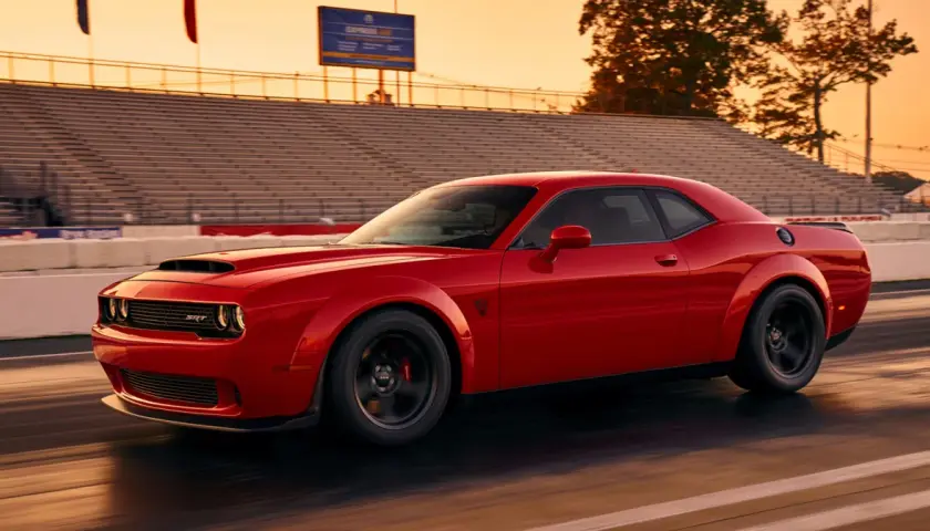 Czerwony Dodge Challenger SRT pędzi po torze wyścigowym podczas zachodu słońca, z trybunami w tle.