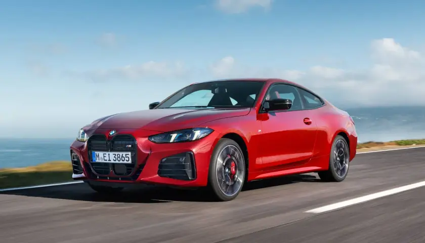 Czerwone coupe BMW M4 na drodze z widokiem na morze i niebo.
