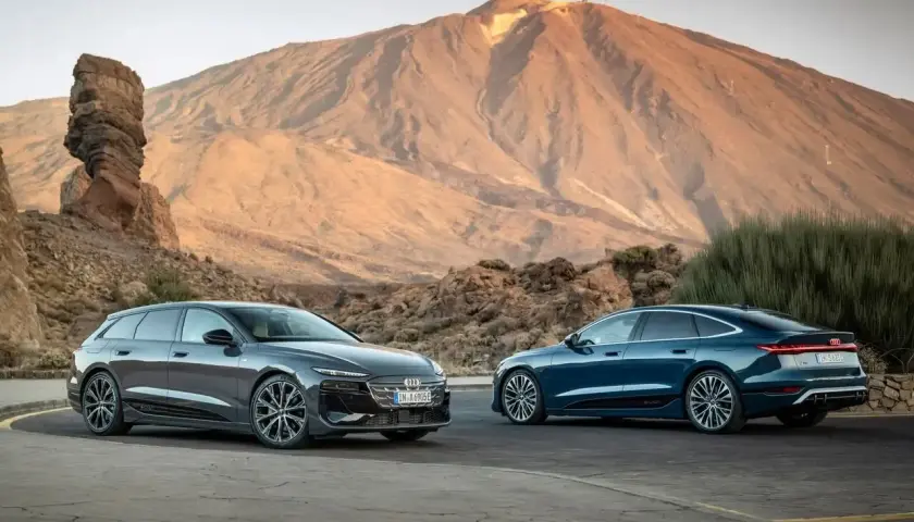 Dwa lśniące Audi, jeden sedan, drugi kombi, na tle majestatycznej góry.