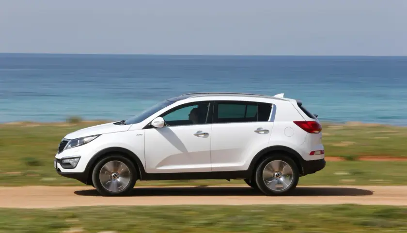Biały Kia Sportage 2012 jedzie po drodze nad morzem.