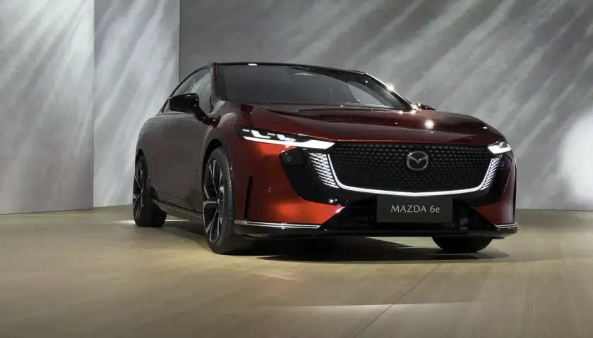 Elegancka, czerwona Mazda 6e prezentuje się na tle nowoczesnej ściany z subtelnymi refleksami światła.