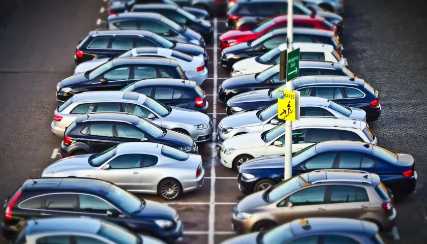 Rząd samochodów na parkingu. Znak "Kasse" sugeruje, że to parking płatny. KNF co to? To może być skrót od nazwy firmy zarządzającej parkingiem.