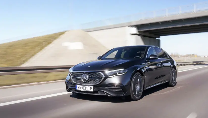 Elegancki, czarny Mercedes E220d mknie autostradą pod betonowym wiaduktem.