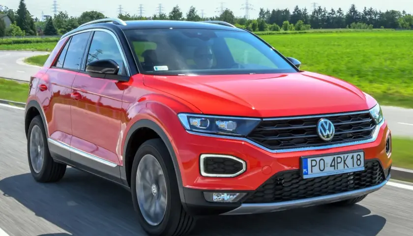 Czerwony volkswagen t-roc używany na drodze, z zielonym polem w tle.