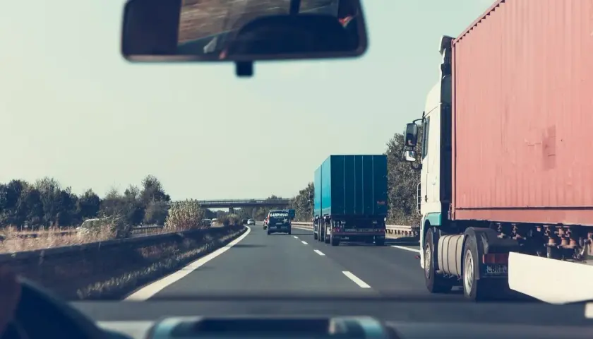 Widok z kabiny samochodu na autostradzie z ciężarówkami i innymi pojazdami.