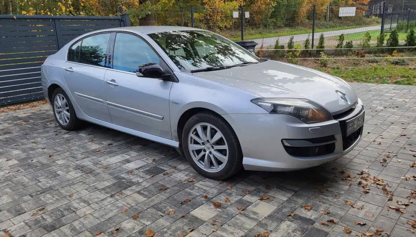 Srebrny sedan Laguna 3 2.0 dCi zaparkowany na podjeździe z kostki brukowej, otoczony jesienną roślinnością.