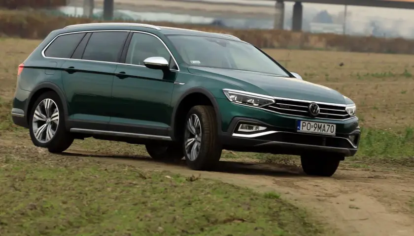 Zielony Passat Alltrack pokonuje piaszczystą drogę wśród traw.