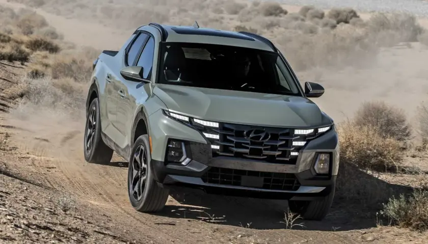 Szary Hyundai Santa Cruz pokonuje pustynny teren, wzbijając tumany kurzu.