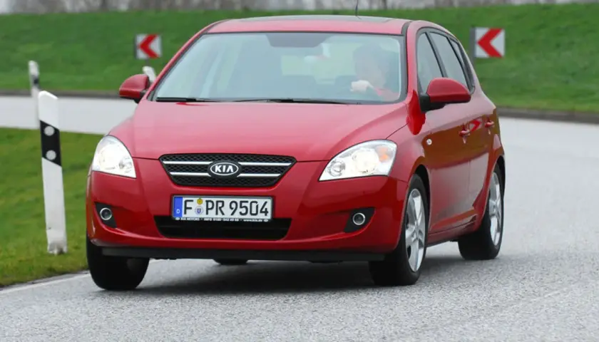 Czerwony Kia Ceed 1.6 CRDi na drodze, z kierowcą za kierownicą.