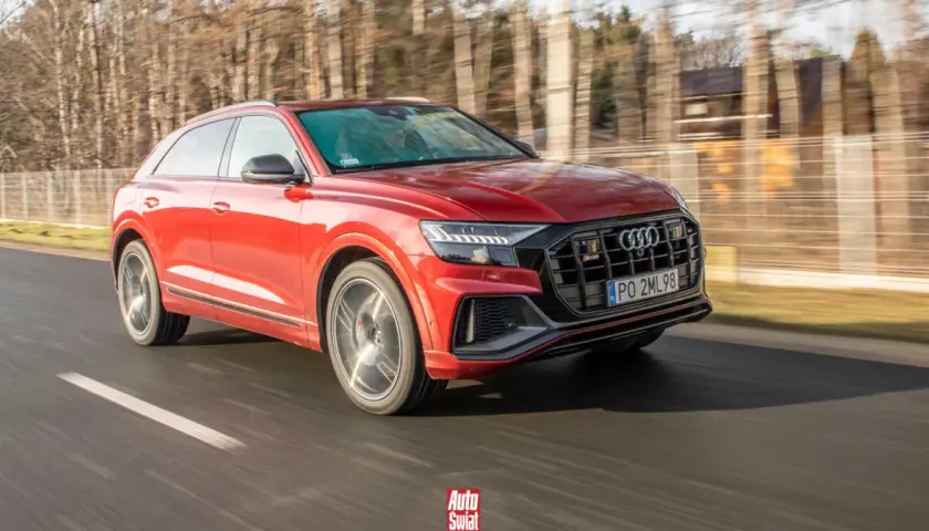 Czerwone Audi SQ8 pędzi po drodze, otoczone rozmazanym lasem.