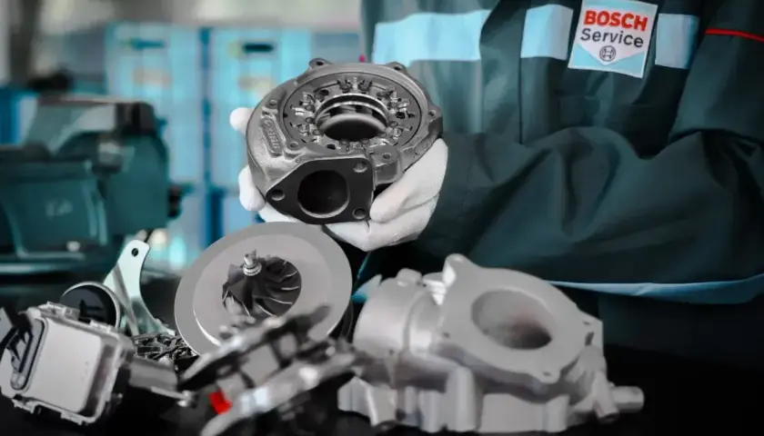 Mechanik w rękawiczkach prezentuje turbosprężarkę p0299. W tle widać inne części i logo Bosch Service.