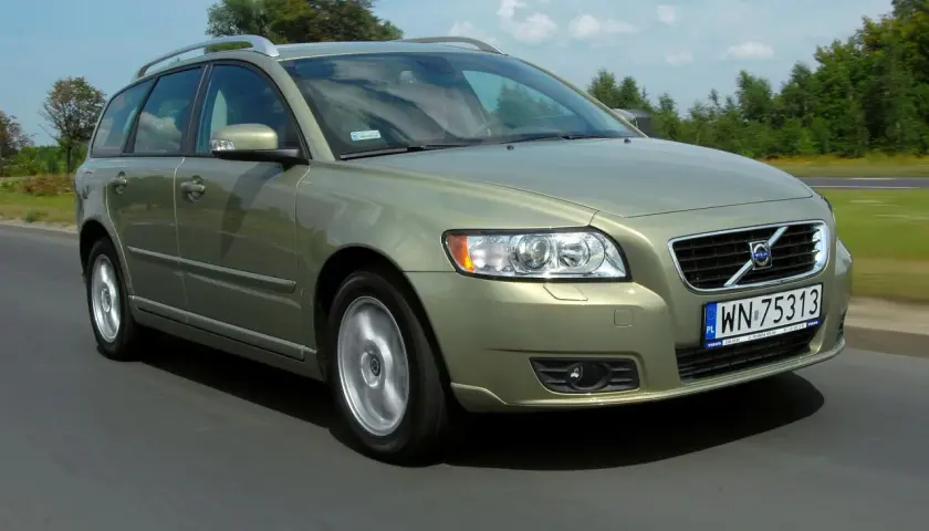 Złoty Volvo V50 2.0D w ruchu drogowym, z zielonymi drzewami w tle.