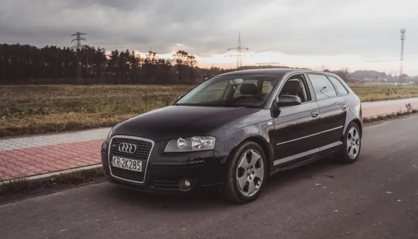 Czarne nowe Audi A3 na tle zachodzącego słońca i linii energetycznych.