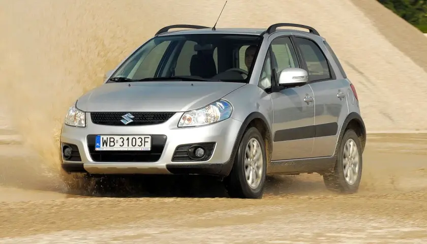 Srebrny Suzuki SX4 1.6 benzyna pokonuje piaszczystą wydmę, wzbijając tumany piasku.