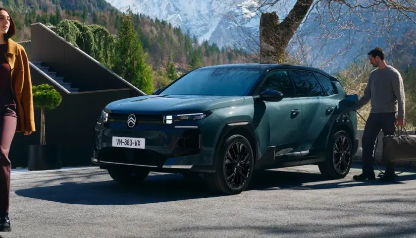 Nowy Citroën C5 Aircross 2025, zielony SUV, ładowany przy górskim domu. Kobieta w płaszczu wychodzi z budynku.