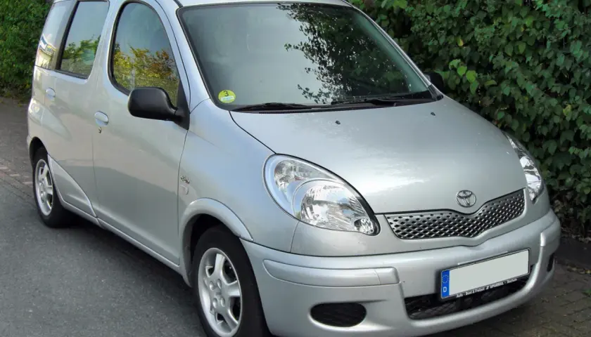 Srebrny Toyota Yaris Verso stoi na tle zielonych krzewów.