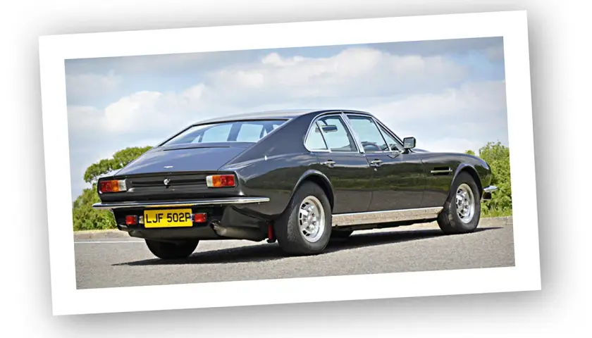 Klasyczny Aston Martin Lagonda z lat 70. na tle błękitnego nieba i zieleni.