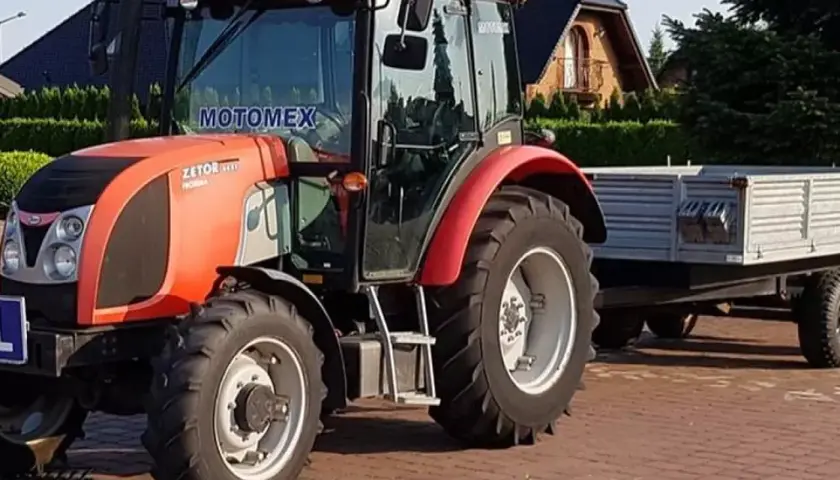 Czerwony Zetor z przyczepą, gotowy do pracy. Posiadanie prawa jazdy na traktor otwiera drogę do wielu możliwości.