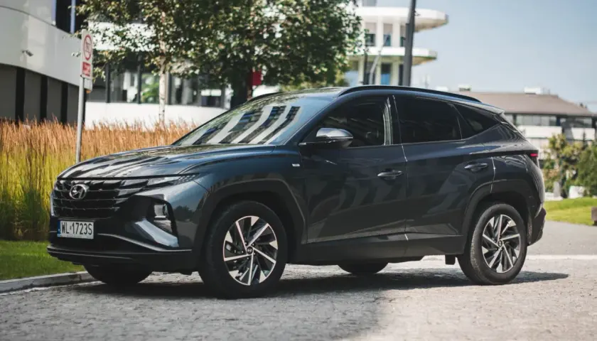 Ciemnoszary Hyundai Tucson 2020 zaparkowany na brukowanej ulicy, z nowoczesnym budynkiem w tle.