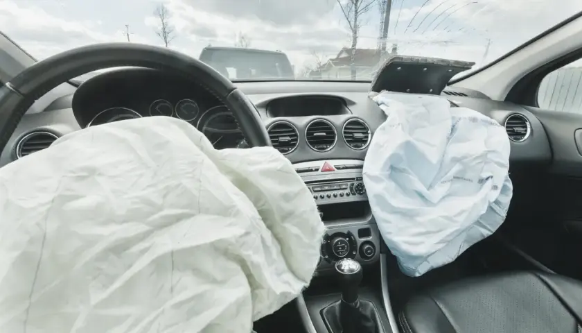 Wnętrze samochodu po wypadku. Rozwinięty **airbag** kierowcy i pasażera, pęknięta przednia szyba.
