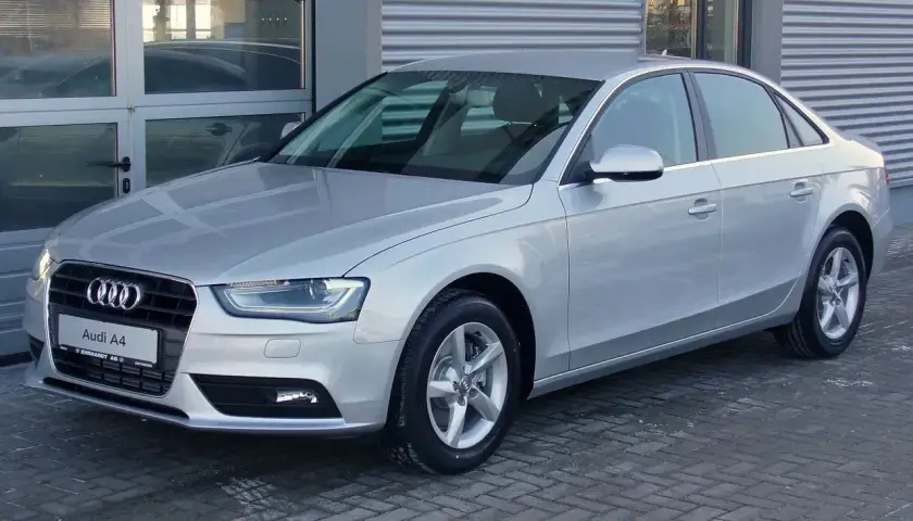 Srebrny Audi A4 B8, model znany z typowych usterek, stoi przed budynkiem.