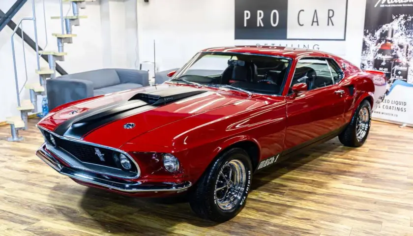 Błyszczący czerwony Ford Mustang Mach 1 z 1969 roku z czarnymi pasami na masce, gotowy do jazdy.