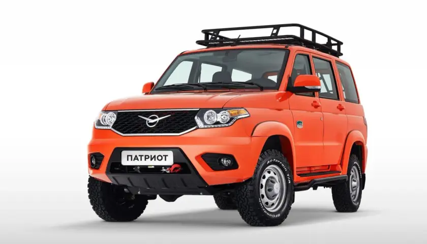 Pomarańczowy UAZ Patriot z bagażnikiem dachowym i wyciągarką na białym tle.