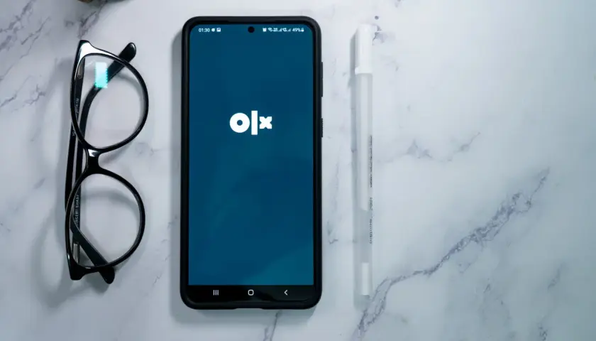 Telefon z aplikacją OLX, okulary i długopis na marmurowym tle. Dowiedz się, jak dodać ogłoszenie na OLX za darmo.