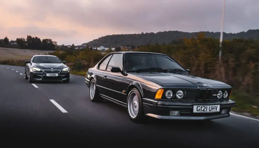 Klasyczne bmw 635 csi i nowszy model jadą drogą o zachodzie słońca.