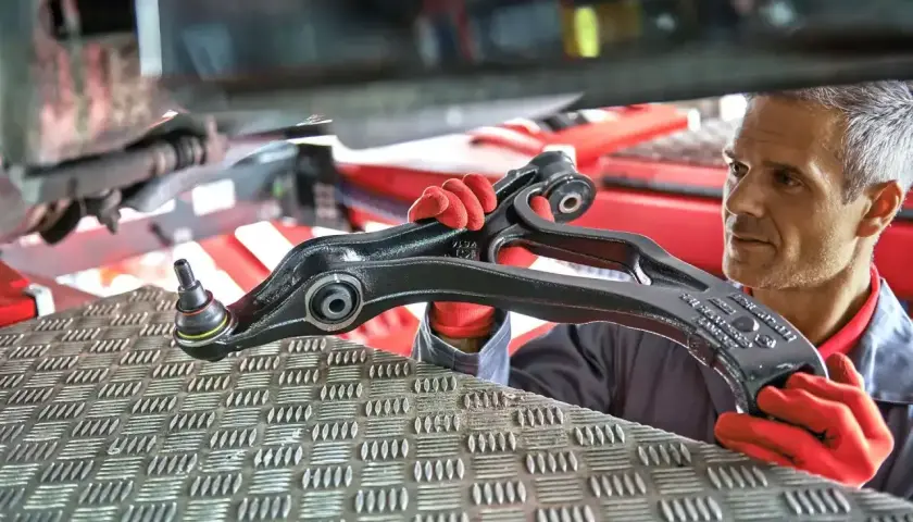 Mechanik w czerwonych rękawiczkach prezentuje element zawieszenia samochodu.