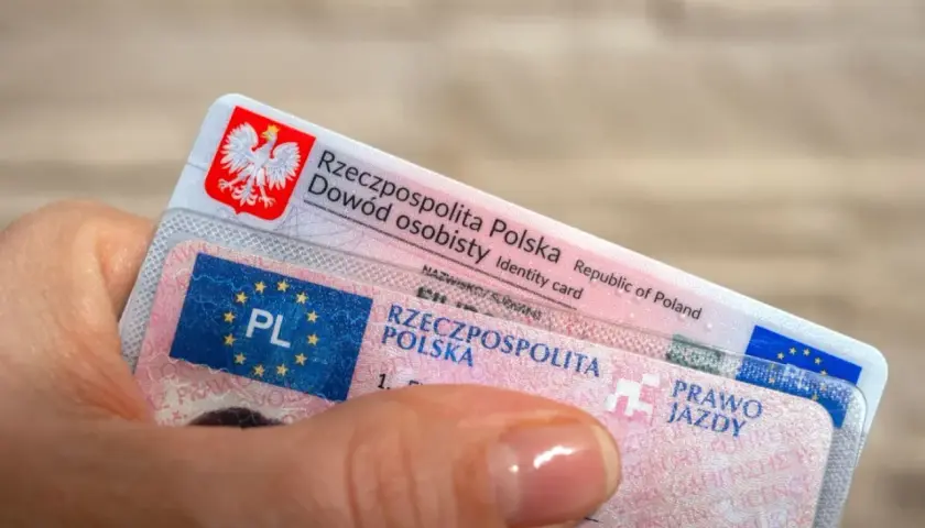 Dłoń trzyma polski dowód osobisty i prawo jazdy. To ważne dokumenty, które pozwalają na swobodne podróżowanie, a prawo jazdy bezterminowe daje spokój na lata.