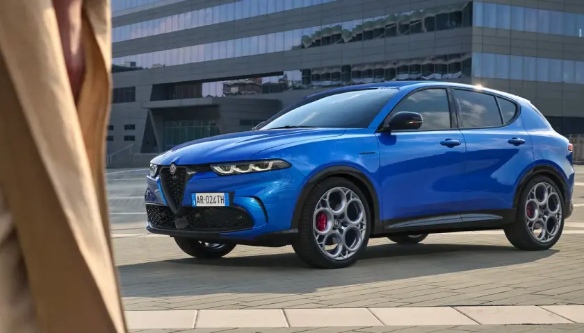 Niebieskie Alfa Romeo Tonale błyszczy na tle nowoczesnego budynku. Sprawdź aktualną alfa romeo tonale cena i odkryj jego możliwości.