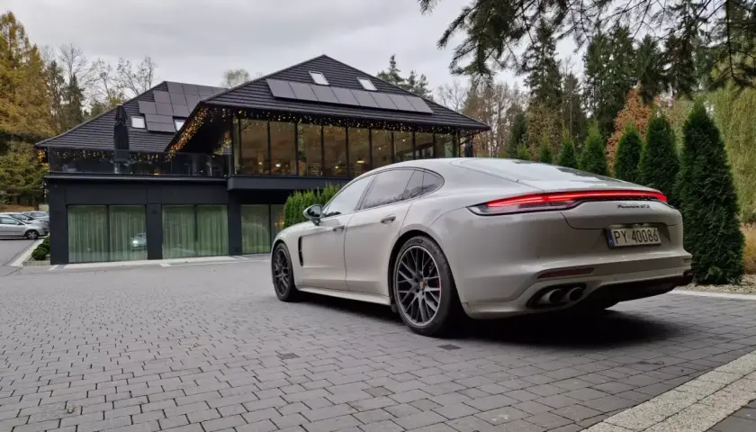 Białe Porsche Panamera GTS przed nowoczesnym budynkiem z panelami słonecznymi. Idealny wybór dla firm ceniących leasing operacyjny.