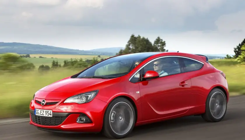 Czerwony Opel Astra J Hatchback pędzi przez malownicze krajobrazy.