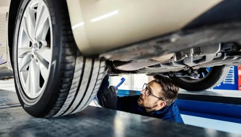 Mechanik z latarką bada podwozie samochodu.