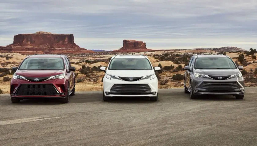 Trzy modele Toyota Sienna 2025 w różnych kolorach stoją na tle pustynnego krajobrazu z formacjami skalnymi.