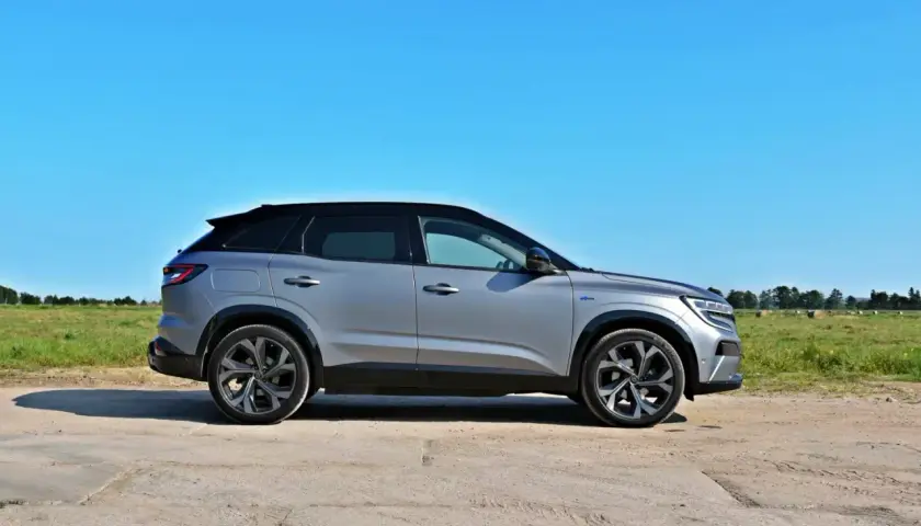 Srebrny Renault Austral z czarnym dachem na tle błękitnego nieba i zielonego pola.
