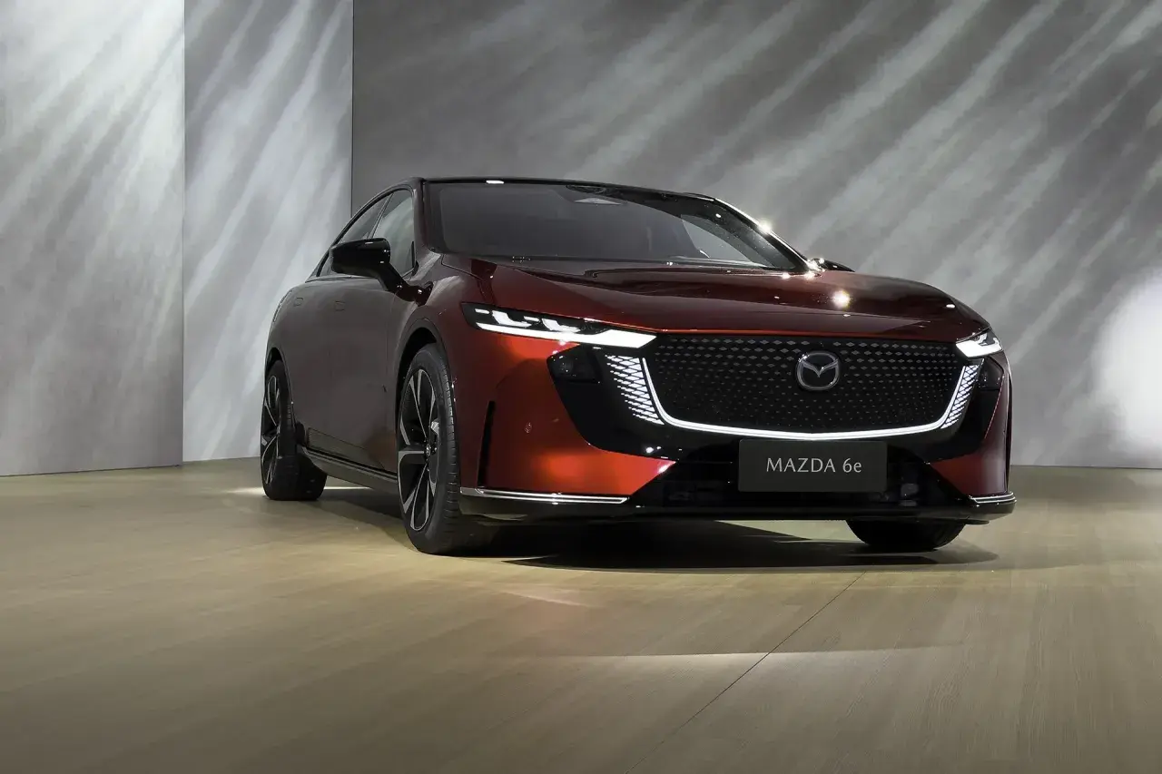 Elegancka, czerwona Mazda 6e prezentuje się na tle nowoczesnej ściany z subtelnymi refleksami światła.
