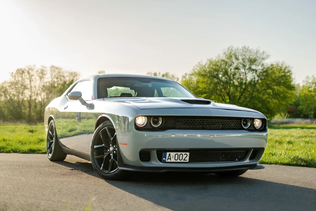 Srebrny Dodge Challenger 5.7 Hemi z czarnymi felgami na tle zielonej łąki i drzew.