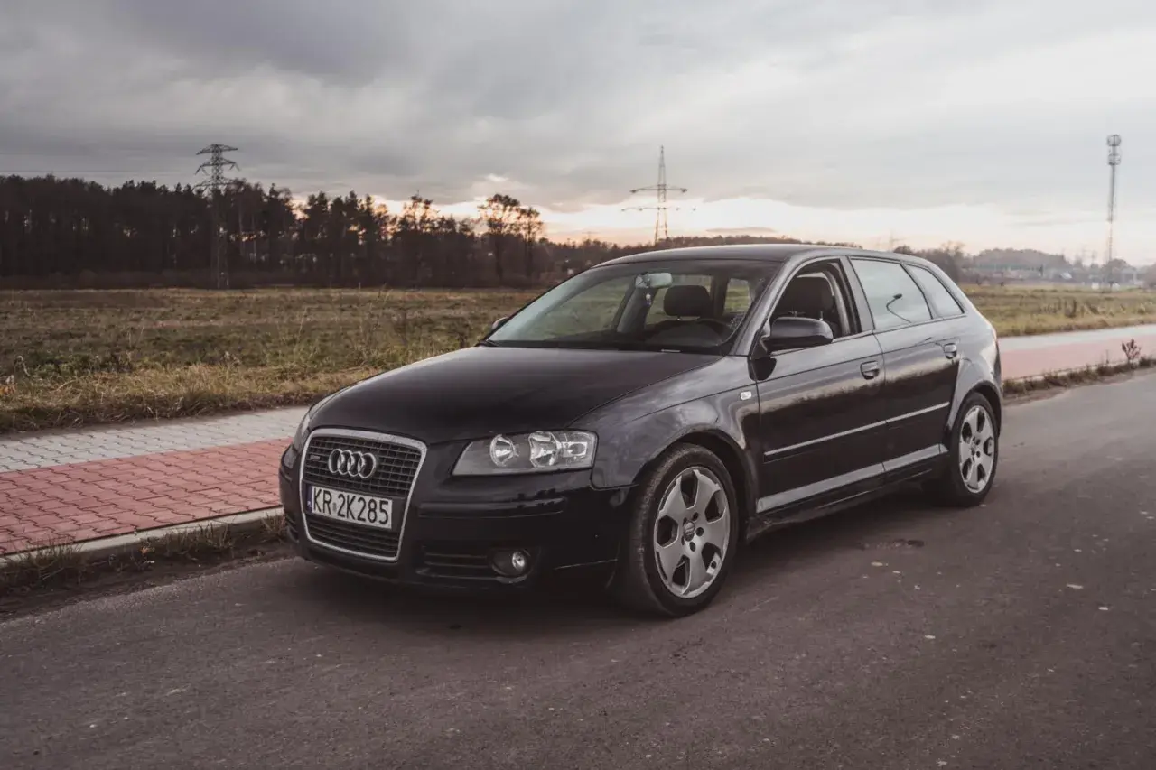Czarne nowe Audi A3 na tle zachodzącego słońca i linii energetycznych.