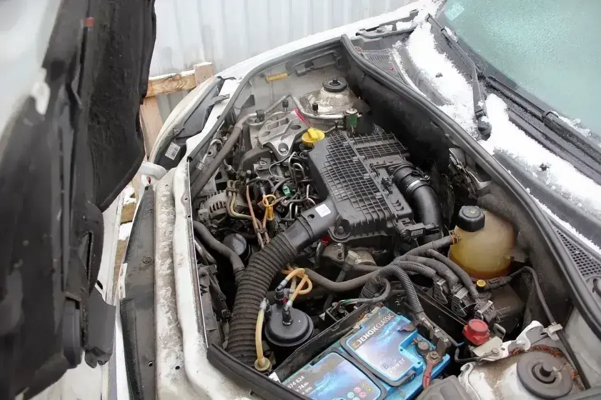 Silnik renault kangoo 1.5 dci z widocznym akumulatorem i przewodami. W tle śnieg na masce i szybie.
