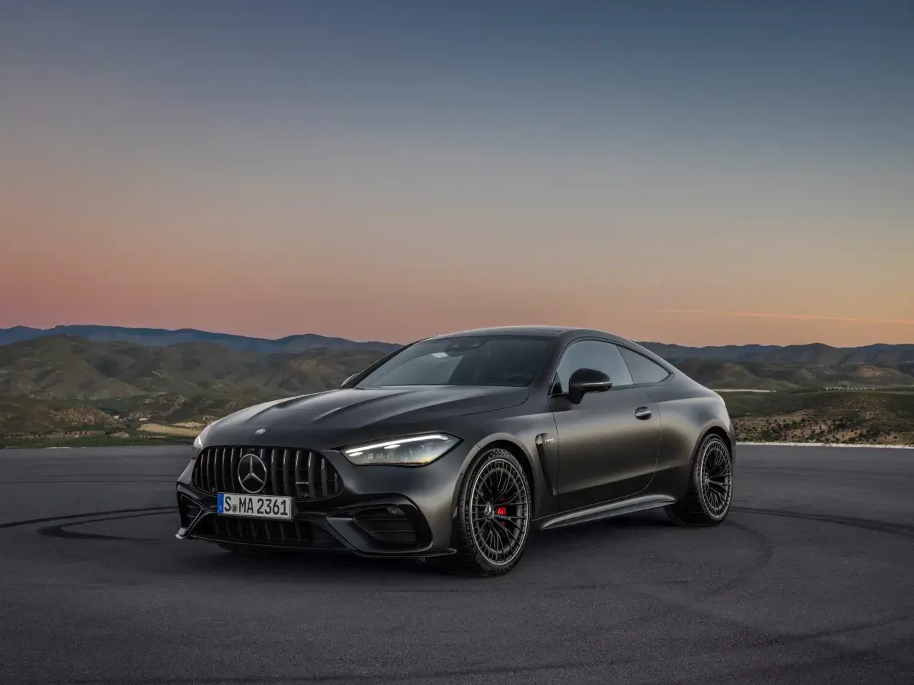 Mroczny Mercedes-AMG GT Coupe na tle zachodzącego słońca i pagórków.