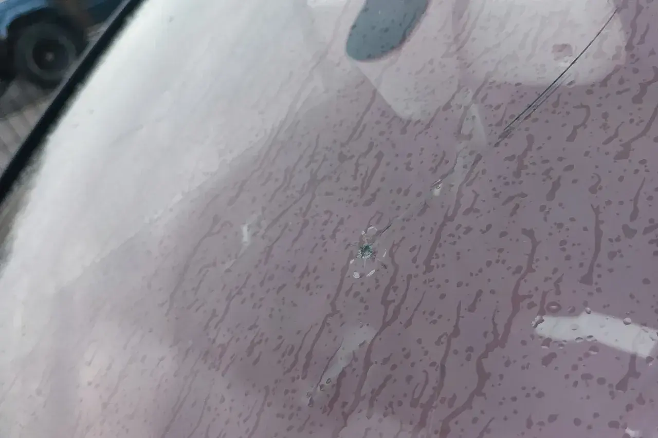 Pęknięta szyba w aucie z widocznym punktowym uszkodzeniem i pajęczyną pęknięć. Krople deszczu spływają po powierzchni.