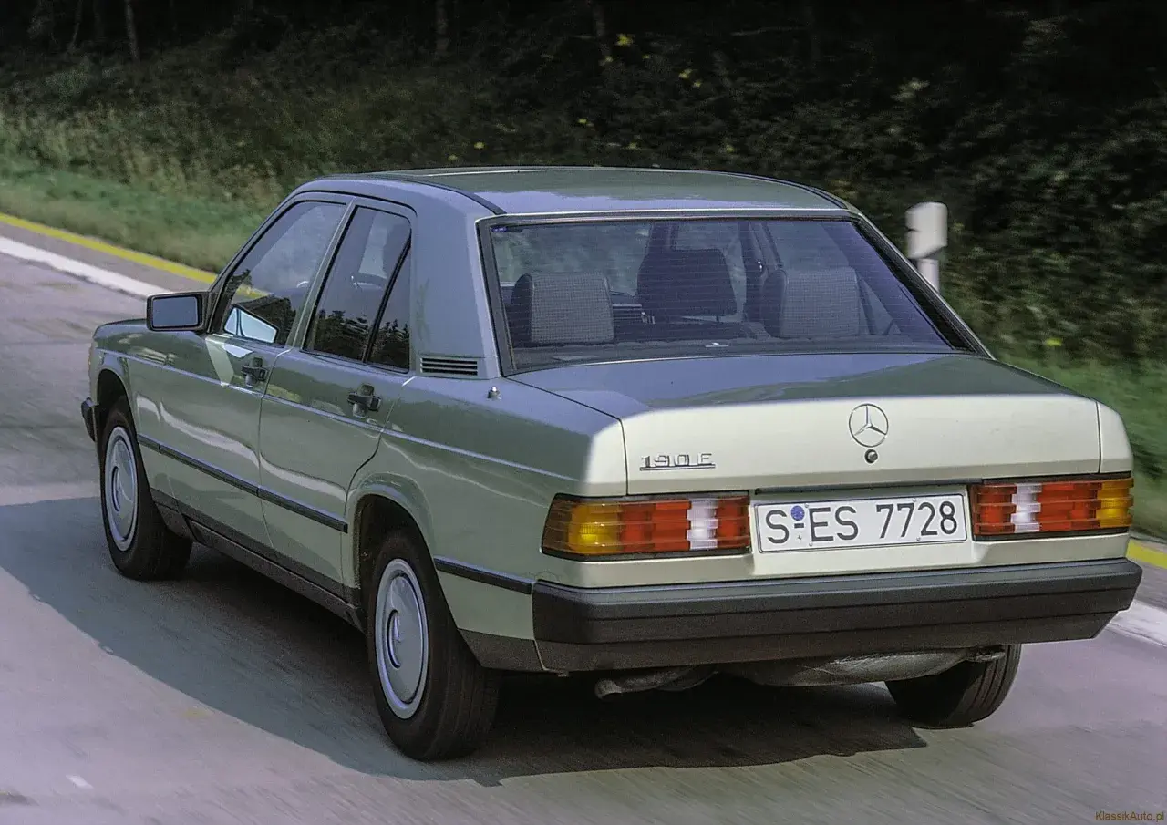 Klasyczny zielony Mercedes 190E z lat 80. sunie po drodze wśród drzew.
