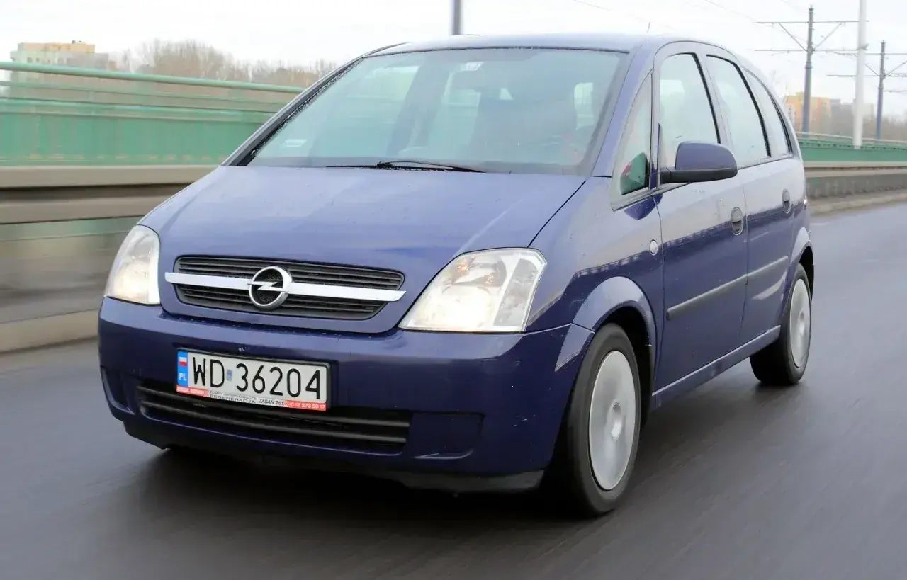 Niebieski Opel Meriva 1.6 benzyna jedzie po mokrej drodze.