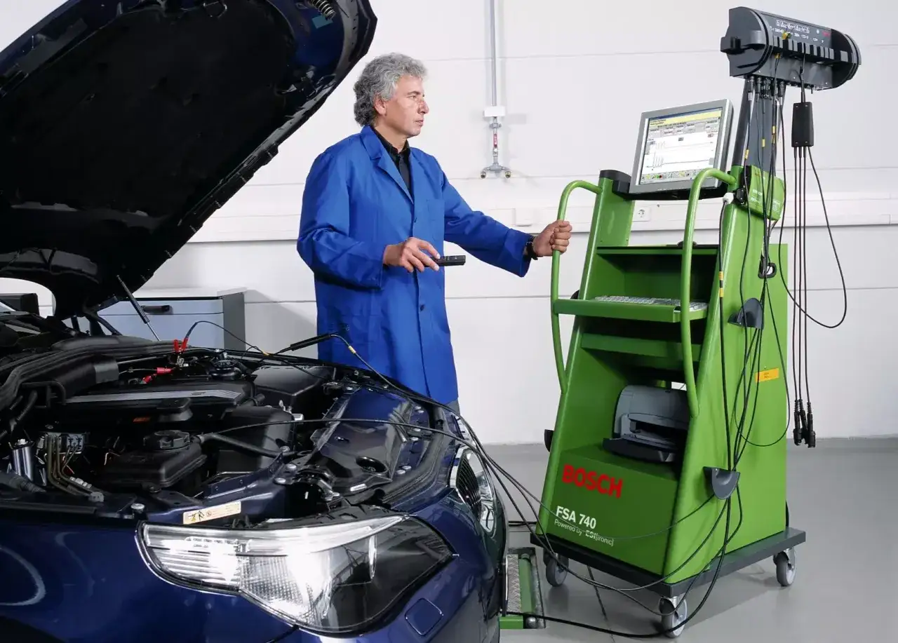 Mechanik z niebieską kurtką używa testera Bosch FSA 740, aby sprawdzić cewkę zapłonową w samochodzie.